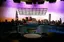 Professional television studio set with scenic backdrop of Seattle cityscape at sunset, featuring circular interview area with patterned chairs and overhead lighting grid for broadcast production