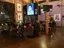 Live event venue with audience seated in industrial loft space featuring exposed brick walls, professional lighting equipment, and multiple monitor displays for multimedia presentations and performances
